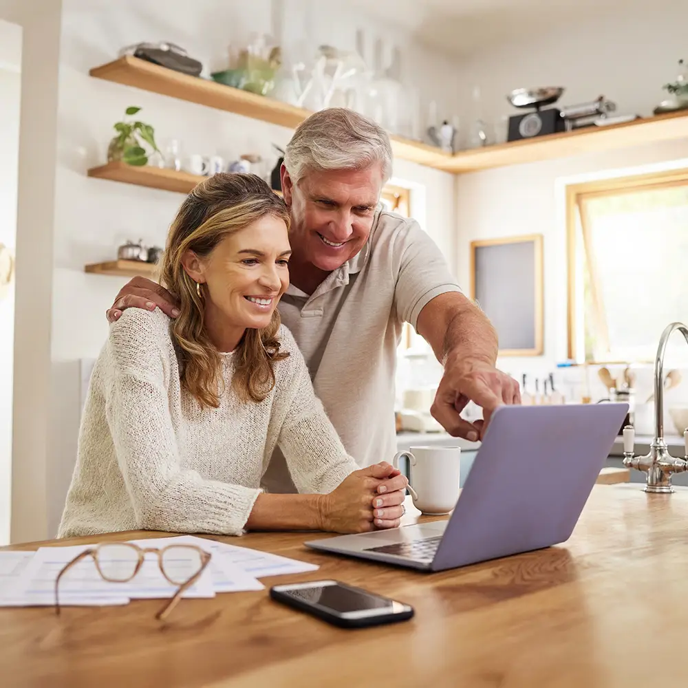 Senior couple using a laptop at home while reviewing insurance documents together