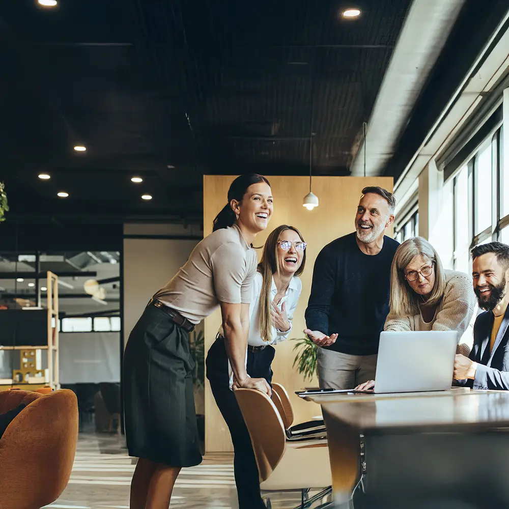 Group of diverse colleagues celebrating a successful project around a laptop in a modern office.