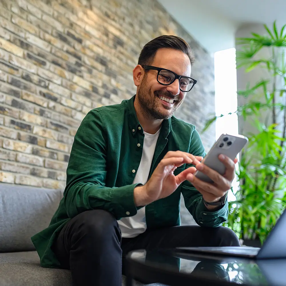 Man using a smartphone while sitting on a sofa in a modern indoor setting.