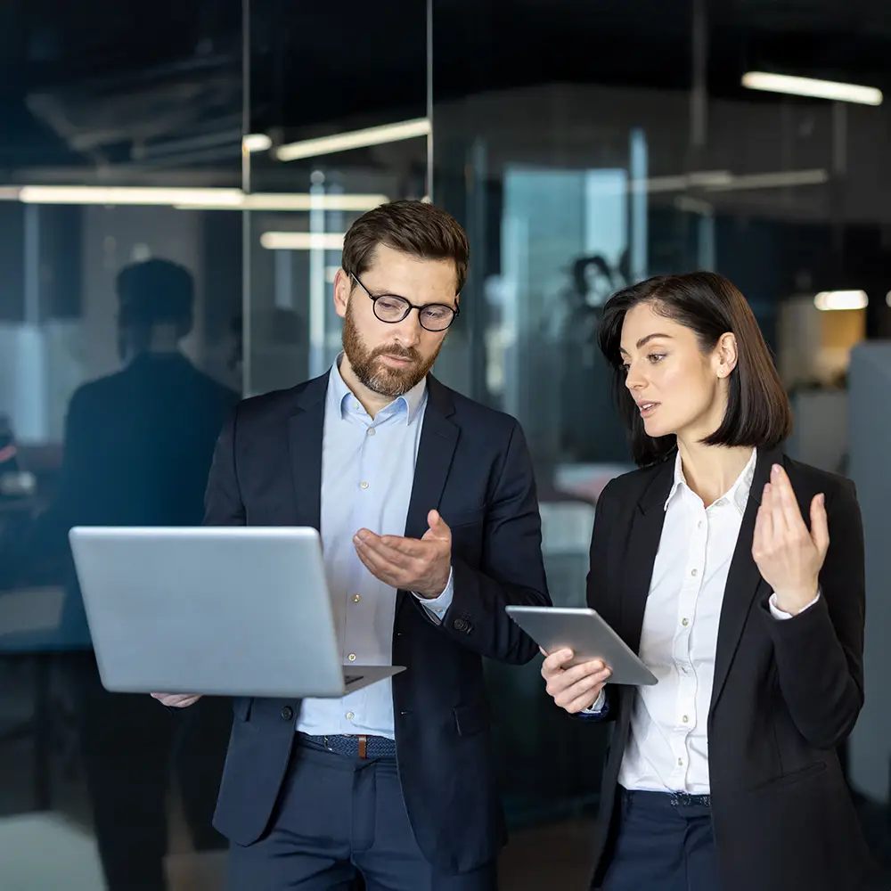 Business professionals reviewing information on a laptop and tablet during a meeting in a modern office setting.